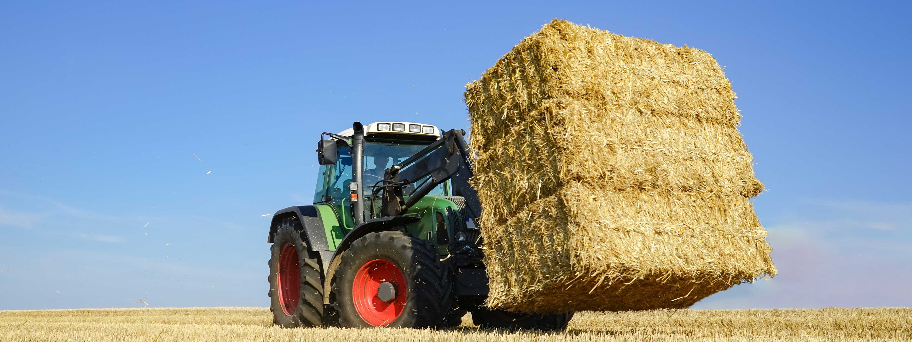Ein Traktor mit drei Stroh-Quaderballen auf einem Feld.